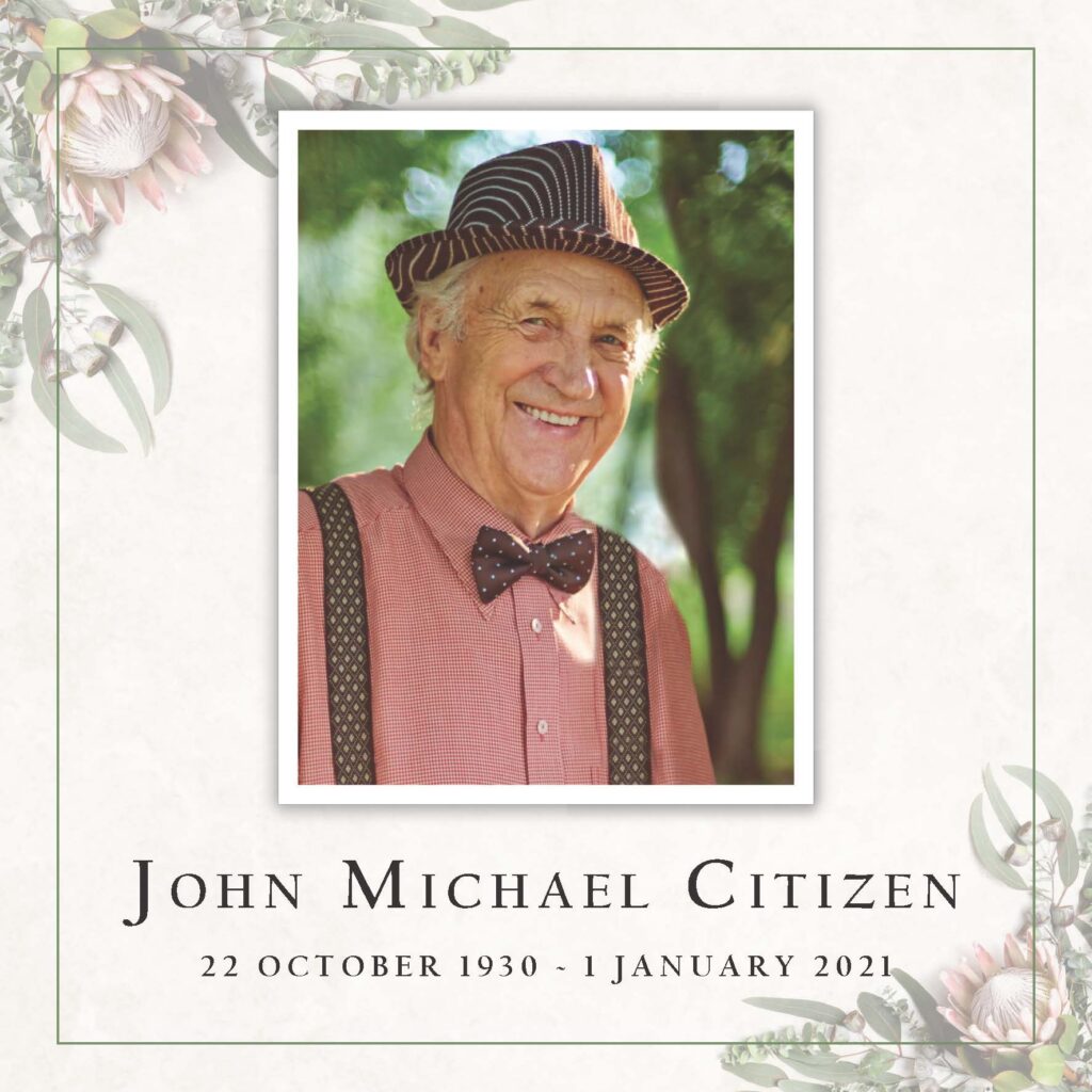 Elderly man in hat and bowtie smiling outdoors.