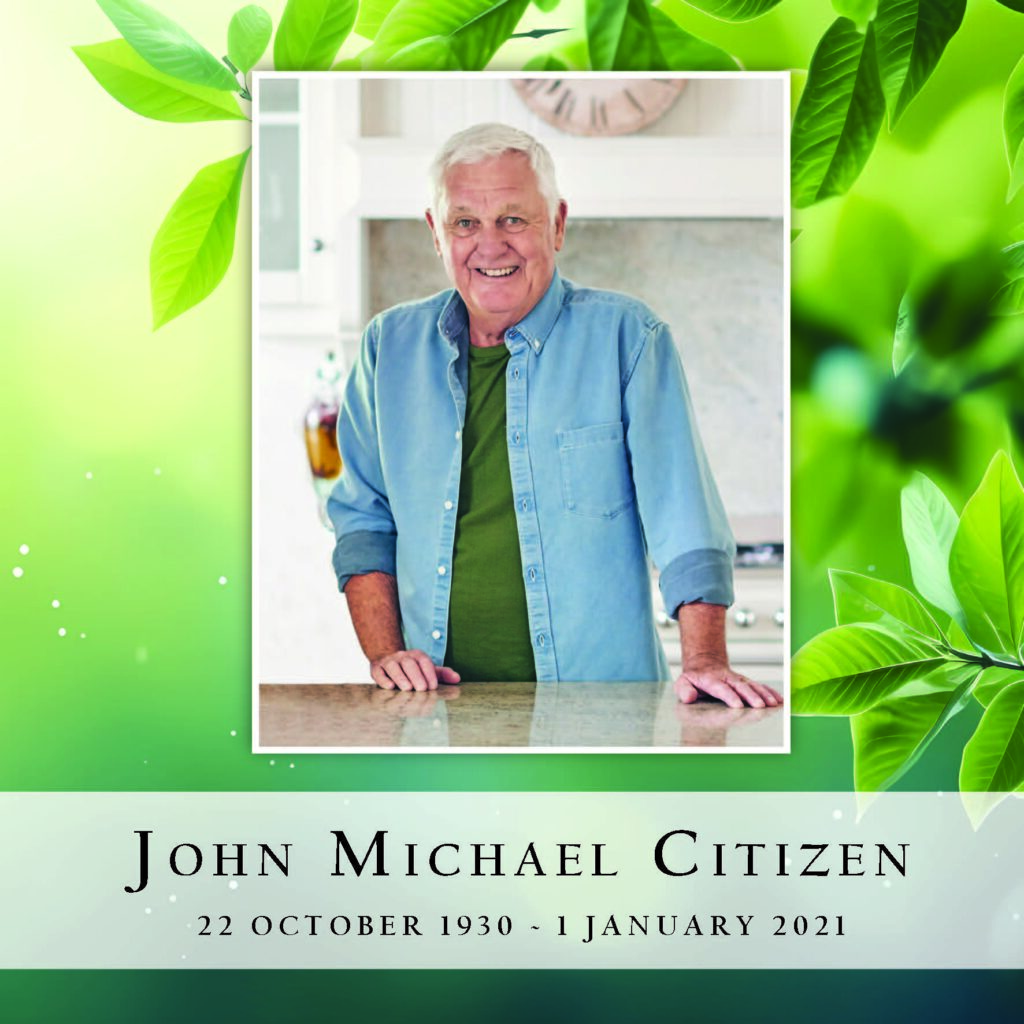 Smiling elderly man in kitchen, green leaf background.